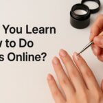 Close-up of a person painting nails with a fine brush during an online nail learning tutorial, showing natural manicure with white nail art.